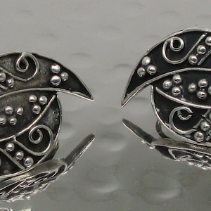 May include: A pair of silver earrings with a swirling, abstract design. The earrings are made of metal and have a dark, oxidized finish.