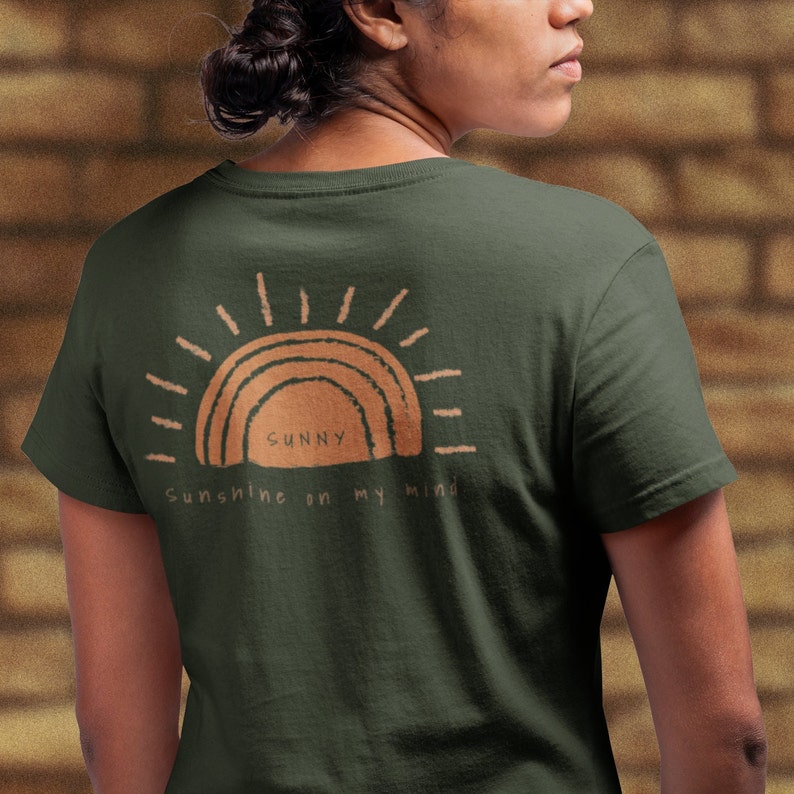 Puede incluir: Una camiseta verde oscuro con un gr&aacute;fico de sol marr&oacute;n y el texto "Sunny Sunshine on my mind".