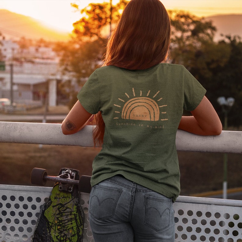 Puede incluir: Una camiseta verde con un gr&aacute;fico de sol y el texto "Sunny Sunshine in my mind".