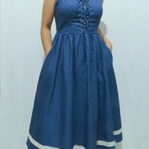 May include: A blue and white polka dot midi dress with a lace-up bodice and white trim around the hem.