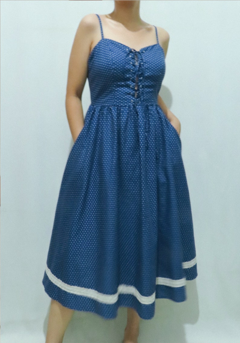May include: A blue and white polka dot midi dress with a lace-up bodice and white trim around the hem.