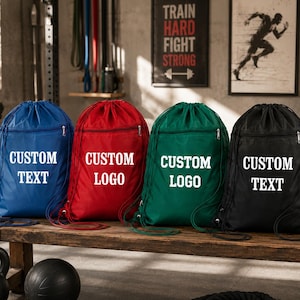May include: Four drawstring backpacks in blue, red, green, and black, each featuring a front zippered pocket and white text. The blue and black bags display the words CUSTOM TEXT, while the red and green bags display the words CUSTOM LOGO.