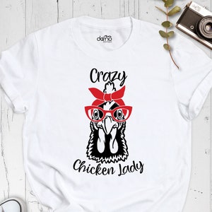 K&ouml;nnte beinhalten: Wei&szlig;es T-Shirt mit einer Schwarz-Wei&szlig;-Illustration eines Huhns mit roter Brille und rotem Bandana. Der Text "Crazy Chicken Lady" ist unter der Illustration aufgedruckt.