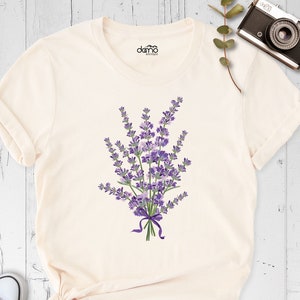 May include: A cream colored t-shirt with a purple lavender flower bouquet graphic. The bouquet is tied with a purple ribbon.