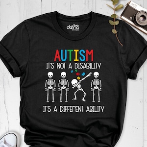 May include: Black t-shirt with a graphic of skeletons and the text "AUTISM IT'S NOT A DISABILITY IT'S A DIFFERENT ABILITY".