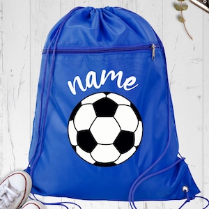 May include: A royal blue drawstring backpack with a soccer ball graphic and the word "name" in white script. The soccer ball is black and white. The bag has a zippered pocket and white sneakers are visible in the bottom left corner.