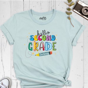 May include: Light blue t-shirt with the text "hello second grade" in colorful letters and a pencil with the text "I'm Emily".