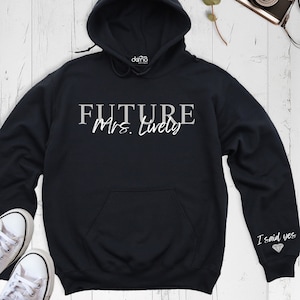 May include: Black hooded sweatshirt with the text "FUTURE Mrs. [Last Name]" in white on the front and "I said yes" with a diamond on the sleeve.
