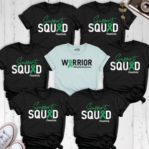 May include: Five black t-shirts with white text and a green ribbon design. The text on four of the shirts reads "Support Squad #TeamEmily". The text on the fifth shirt reads "Warrior #KidneyDiseaseAwareness".