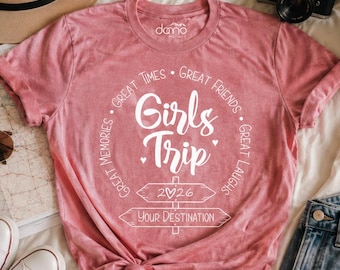 May include: A dusty rose short-sleeve t-shirt featuring white text that reads Girls Trip, Great Times, Great Friends, Great Memories, Great Laughs, 2026, and Your Destination, with a graphic of two directional signs and small hearts.