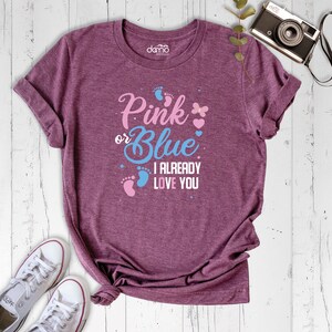 May include: A heather purple t-shirt with the text "Pink or Blue I Already Love You" in blue and pink lettering. The shirt features a pink butterfly and pink and blue footprints.