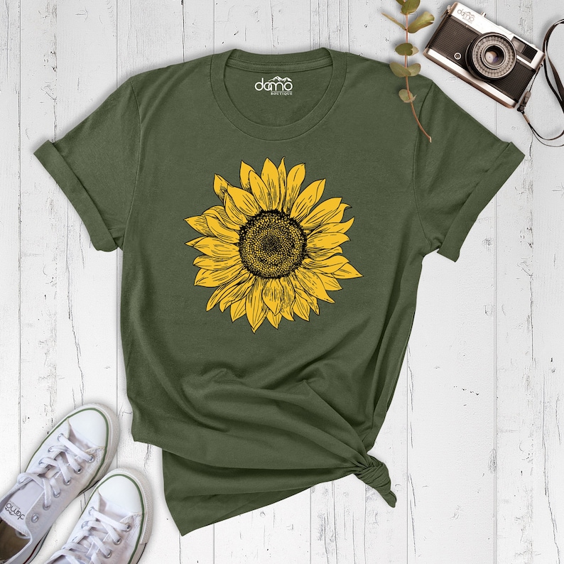 以下が含まれることがあります： 黄色のひまわり柄の緑色のTシャツ。クルーネックと半袖です。