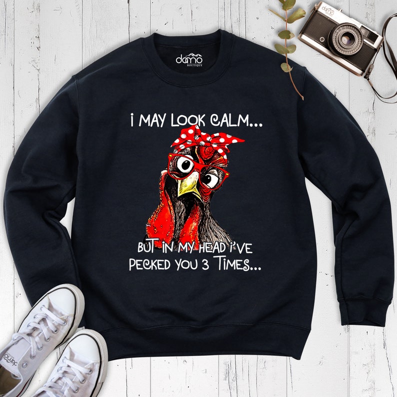 May include: Black sweatshirt with a red and white illustration of a chicken wearing glasses and a red bandana with white polka dots. The text "I may look calm... But in my head I've pecked you 3 times..." is printed on the sweatshirt.