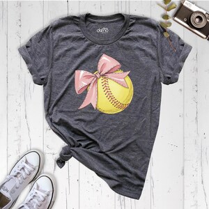 May include: A gray t-shirt with a yellow softball with a pink bow on it.