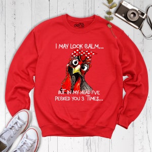 May include: Red sweatshirt with a graphic of a chicken wearing glasses and a red bandana. The text on the sweatshirt reads "I may look calm... But in my head I've pecked you 3 times..."