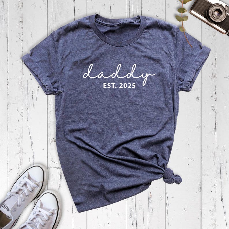 May include: A dark blue t-shirt with the text "daddy est. 2025" in white.