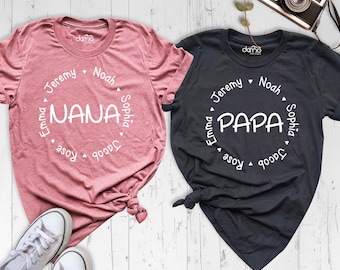 May include: A mauve t-shirt with the text NANA and a black t-shirt with the text PAPA, both featuring a circular arrangement of the names Jeremy, Noah, Sophia, Jacob, Rose, and Emma in white print, accompanied by a vintage camera.