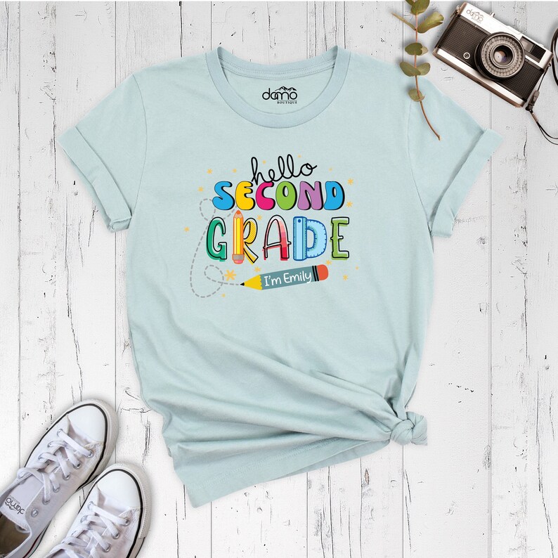 May include: Light blue t-shirt with the text "hello second grade" in colorful letters and a pencil with the text "I'm Emily".