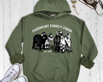 Może przedstawiać: Oliwkowa bluza z kapturem z białym nadrukiem graficznym przedstawiającym cztery koźlęta. Tekst nad koźlętami brzmi FAIRMONT FAMILY FARM, a tekst poniżej Est. 1997. Bluza ma długie rękawy i przednią kieszeń typu kangurka.