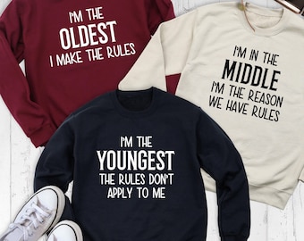 May include: Three crewneck sweatshirts in maroon, cream, and navy blue. The maroon sweatshirt says I'M THE OLDEST I MAKE THE RULES. The cream sweatshirt says I'M IN THE MIDDLE I'M THE REASON WE HAVE RULES. The navy sweatshirt says I'M THE YOUNGEST THE RULES DON'T APPLY TO ME.