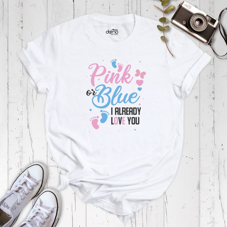 May include: White t-shirt with the text "Pink or Blue I Already Love You" in black, pink, and blue. The text is surrounded by pink and blue footprints and hearts.
