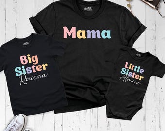 May include: A black t-shirt with the word Mama in pastel letters, a black t-shirt with Big Sister Rowena in pastel letters, and a black baby bodysuit with Little Sister Almira in pastel letters, all featuring short sleeves.