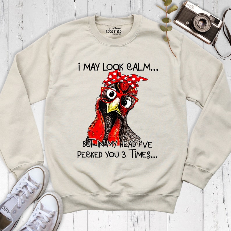 May include: A beige sweatshirt with a graphic of a cartoon chicken wearing red glasses and a red and white polka dot bandana. The text on the sweatshirt reads "I may look calm... But in my head I've pecked you 3 times..."
