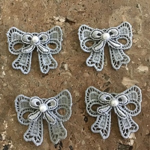 May include: Four grey lace bows with a pearl embellishment in the centre of each bow.