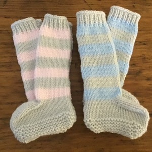 May include: Two pairs of knitted baby socks. One pair features pink and grey stripes, the other blue and grey stripes. The socks are handmade with a ribbed cuff and a solid grey foot.