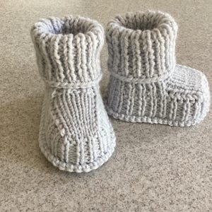 Könnte beinhalten: Ein Paar graue gestrickte Babyschuhe mit Umschlag.