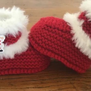 Könnte beinhalten: Rote gestrickte Babyschuhe mit weißem Fellbesatz und einer Weihnachtsmann-Applikation.