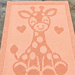 May include: A rectangular peach-coloured knitted blanket featuring a central graphic of a giraffe with a spotted body and two small hearts on either side. The blanket has a textured knit border framing the giraffe design in the centre.