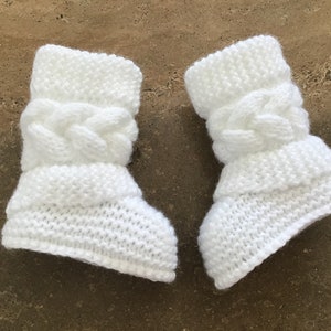 May include: A pair of white knitted baby booties with a cable knit design.