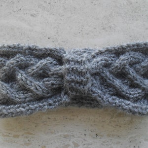 May include: Gray knitted headband with a bow design. The headband is made of a soft, textured yarn.