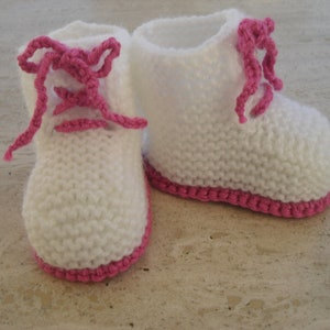 Op de afbeelding: Een paar witte gebreide babyschoentjes met roze veters en roze bies.