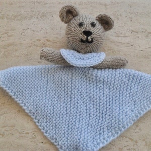 May include: A knitted baby comforter toy, featuring a teddy bear head and arms in tan, with black embroidered details. The attached blanket is light blue and triangular. The soft toy is designed to provide comfort to babies and young children.