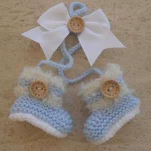 Può includere: Un paio di scarpine per neonato in maglia blu e bianca con un fiocco bianco e bottoni di legno che dicono "È un maschio!"
