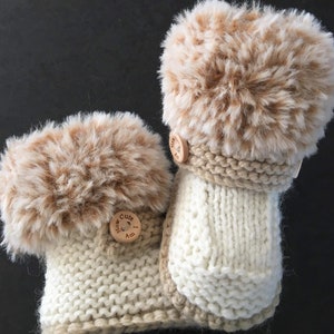 May include: A pair of knitted baby booties with faux fur trim and wooden buttons. The buttons have the text "How Cute I Am" on them.
