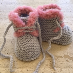 Op de afbeelding: Een paar grijze gebreide babyschoentjes met roze bontbeslag en veters.