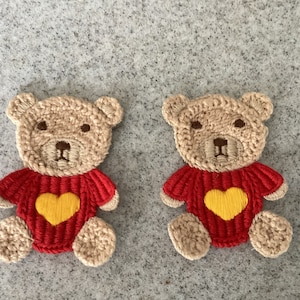May include: Two brown crocheted teddy bears wearing red jumpers with yellow hearts.