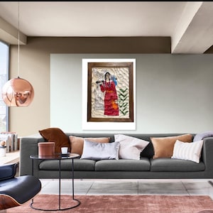 May include: A framed artwork depicting a figure in a red garment, holding an object, with a backdrop of white and green elements. The artwork is displayed above a gray sofa with various pillows, set in a modern living room.
