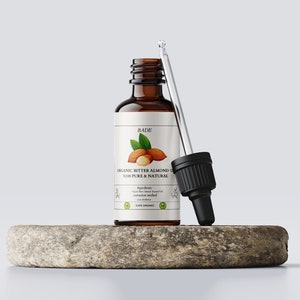 Op de afbeelding: Een bruine glazen fles met een druppelaar gevuld met biologische bittere amandel olie. Het etiket vermeldt "BADE BIOLOGISCHE BITTER AMANDEL OLIE 100% ZUIVER & NATUURLIJK".