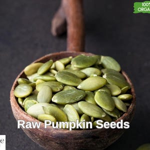 May include: A wooden bowl filled with raw, green pumpkin seeds. The bowl is labelled "Raw Pumpkin Seeds" and has a green sticker that says "100% Organic".