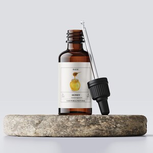 Peut inclure: Une bouteille en verre brun avec un compte-gouttes remplie d'huile essentielle de miel. L'étiquette indique "BADE" et "HONEY Essential Fragrance Oil 100% PURE & NATURAL".