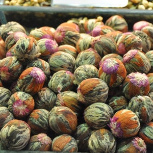 May include: A close-up of a large bowl filled with green, brown, and pink tea buds. The tea buds are arranged in a random pattern and are ready to be brewed.