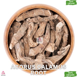 May include: A wooden bowl filled with dried Acorus calamus root. The root is light brown and has a slightly wrinkled texture. The bowl is sitting on a white background. The text "100% Organic" is written on a green label in the upper right corner of the image. The text "ACORUS CALAMUS ROOT" is written in black letters below the bowl. The text "100% ORGANIC" is written on a green label in the lower right corner of the image.