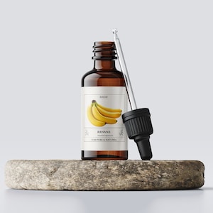 K&ouml;nnte beinhalten: Eine braune Glasflasche mit Tropfer, gef&uuml;llt mit Bananen-Duft&ouml;l. Das Etikett tr&auml;gt die Aufschrift "BADIE" und "BANANA Essential Fragrance Oil 100% PURE & NATURAL". Auf dem Etikett ist eine Bananenstaude abgebildet.
