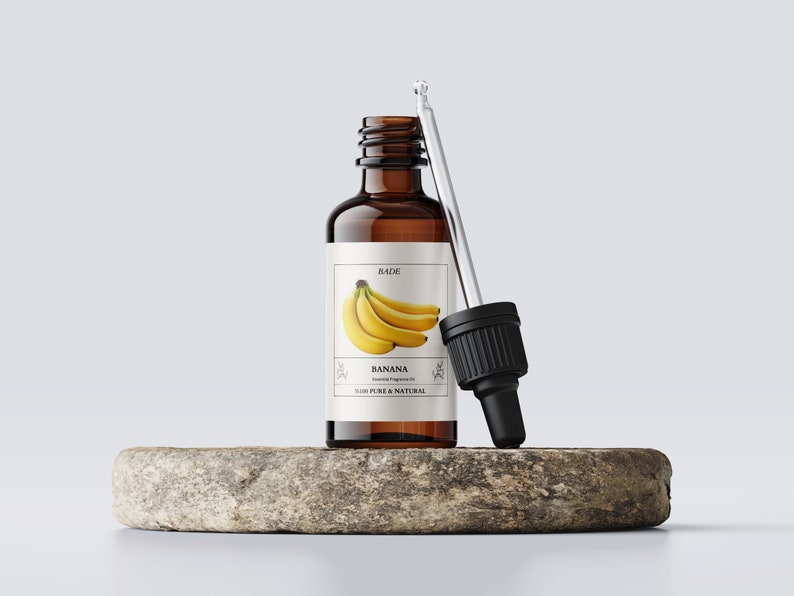 K&ouml;nnte beinhalten: Eine braune Glasflasche mit Tropfer, gef&uuml;llt mit Bananen-Duft&ouml;l. Das Etikett tr&auml;gt die Aufschrift "BADIE" und "BANANA Essential Fragrance Oil 100% PURE & NATURAL". Auf dem Etikett ist eine Bananenstaude abgebildet.