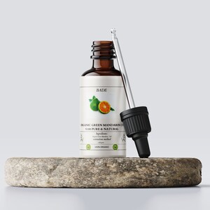 以下が含まれることがあります： 緑のマンダリンオイルが入った茶色のガラス瓶とスポイト。瓶には「BADE ORGANIC GREEN MANDARIN OIL 100% PURE & NATURAL」とラベルが貼られており、緑のマンダリンのイラストが描かれています。