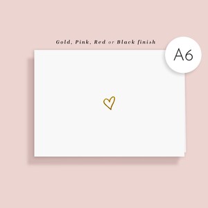 May include: A6 white card featuring a gold heart illustration. The card is set against a light pink backdrop. Text at the top reads "Gold, Pink, Red or Black finish". A white circle with "A6" is in the upper right corner.